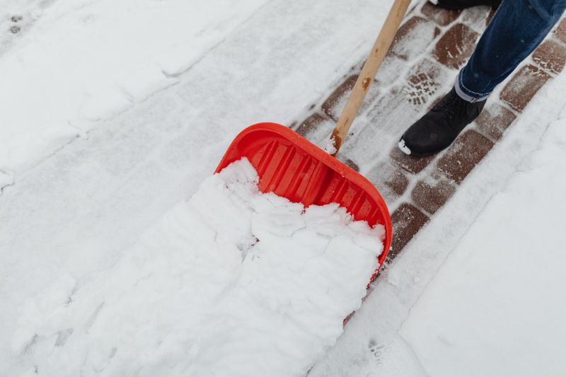 Red snow shovel clearing fresh snow from a walkway